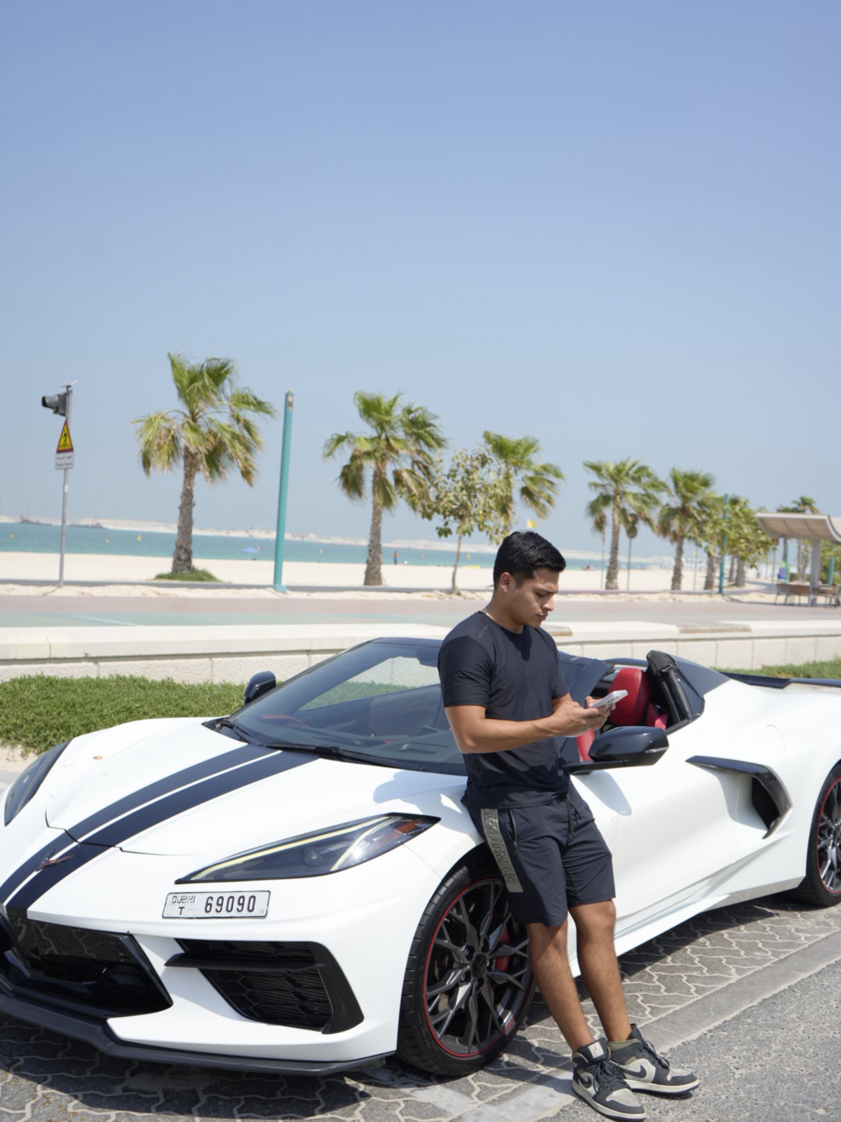 Isaac junto a un auto deportivo, con la playa al fondo